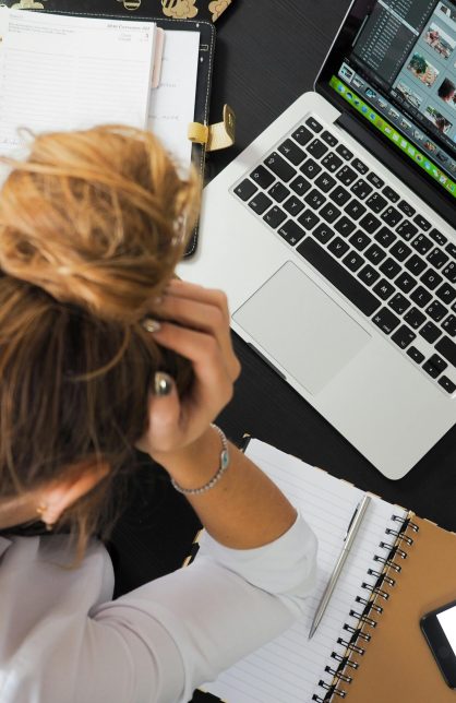 Overhead view of a stressed woman working at a desk with a laptop, phone, and notebooks.